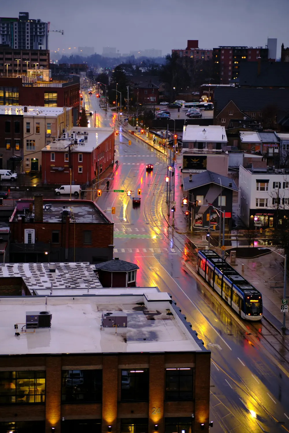 ION light rail train travelling along a wet King Street in Kitchener at dusk, seen from above