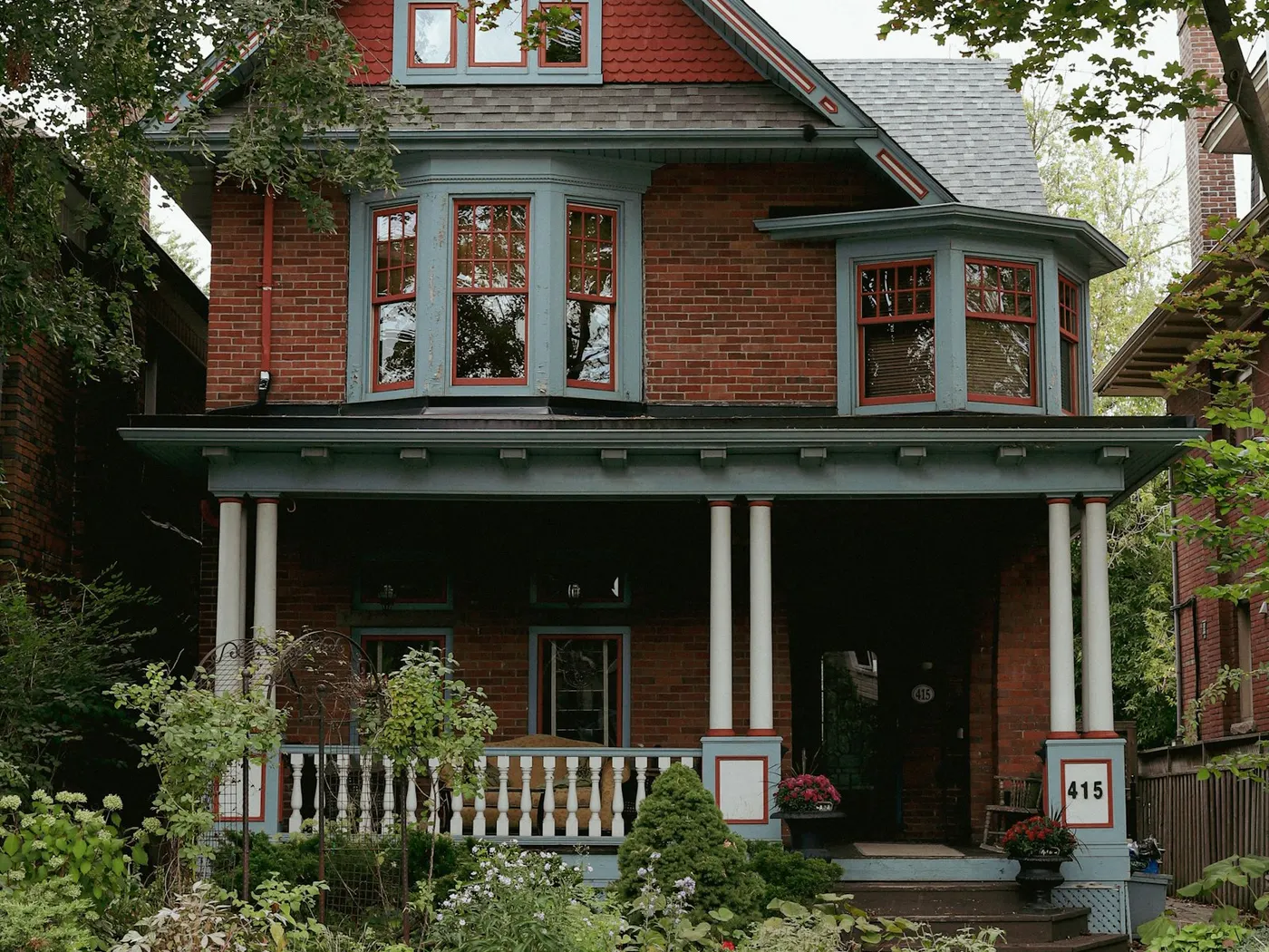 Red brick Victorian house with a wide front porch and garden in Toronto, Ontario