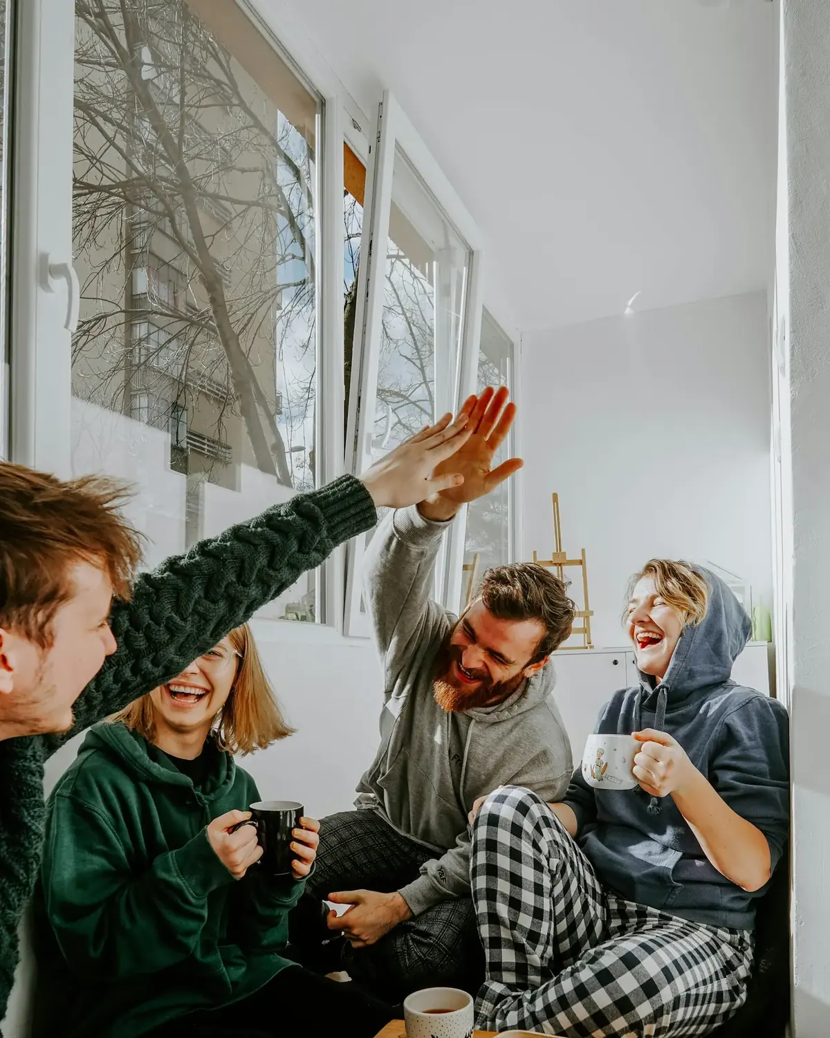 Four friends laughing and high-fiving over coffee