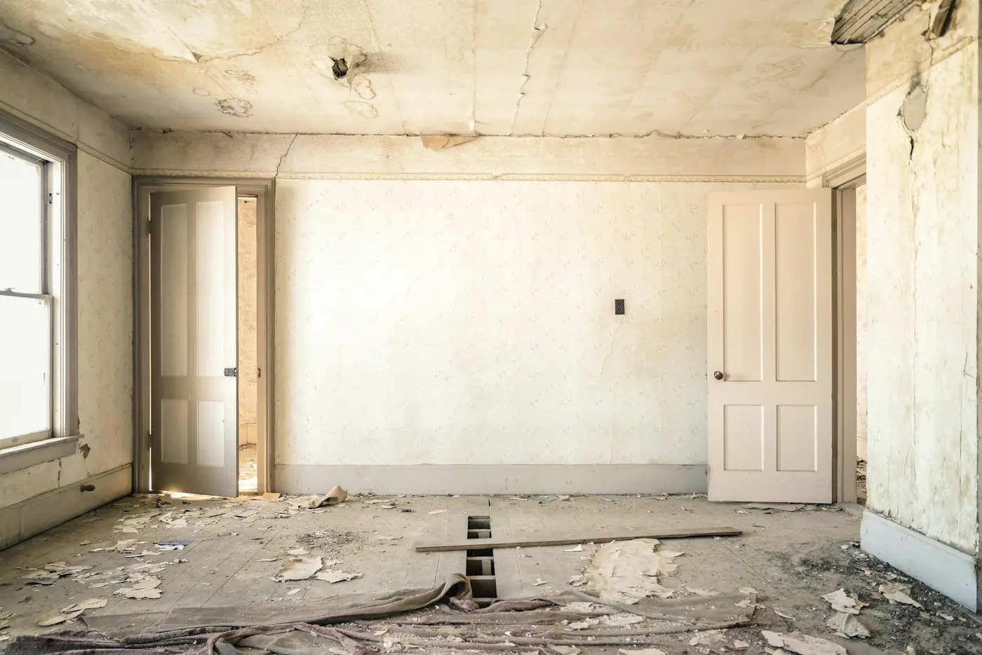 Empty room with worn, damaged floors and bare walls in a house being sold as-is