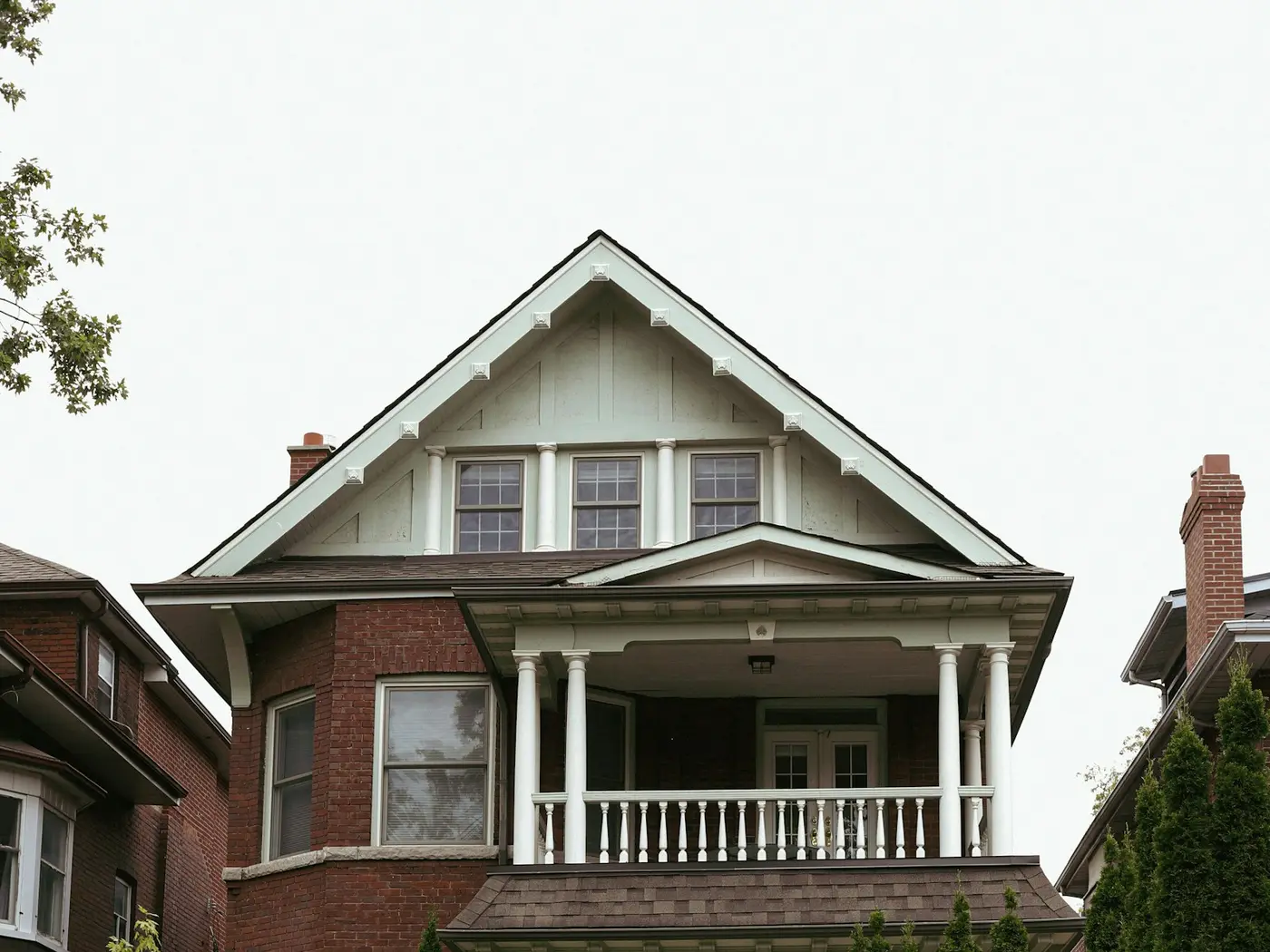 Two-storey brick house with a white front porch and evergreen shrubs