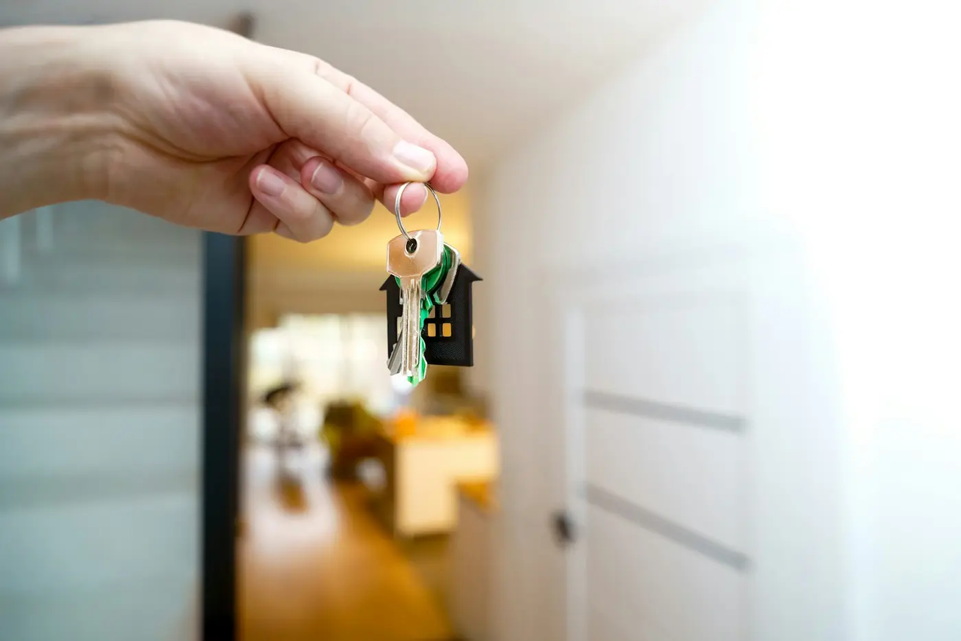 Hand holding a set of keys with a house keychain inside a rental unit