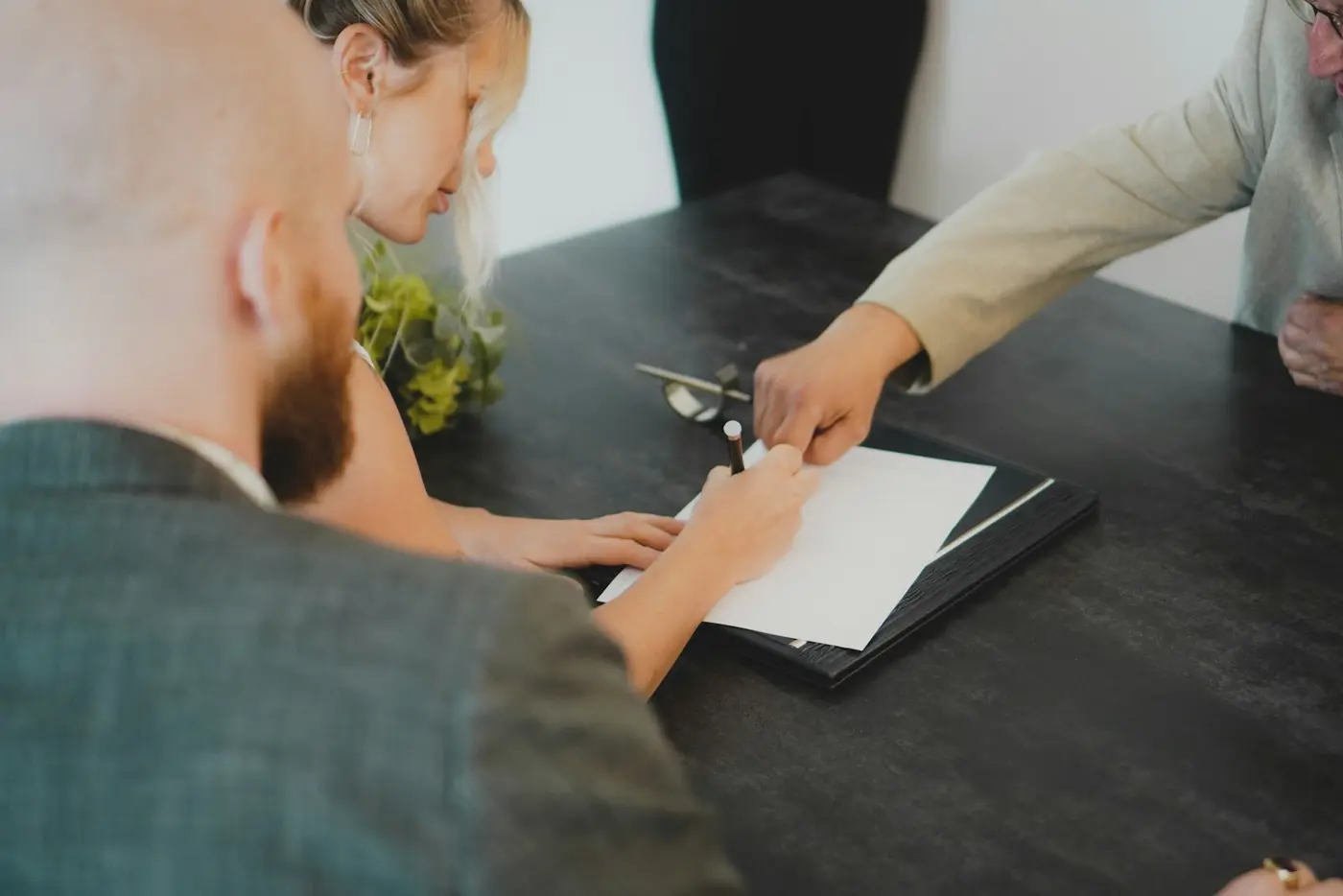 Couple signing an agreement at a desk while a lawyer points to the signature line